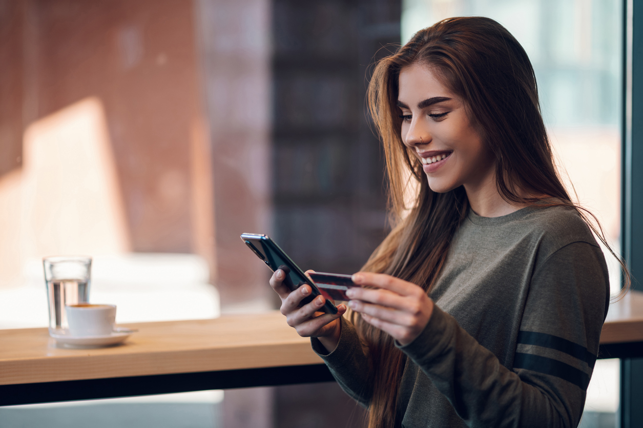Mujer usando un teléfono inteligente y una tarjeta de crédito para comprar en línea en un café