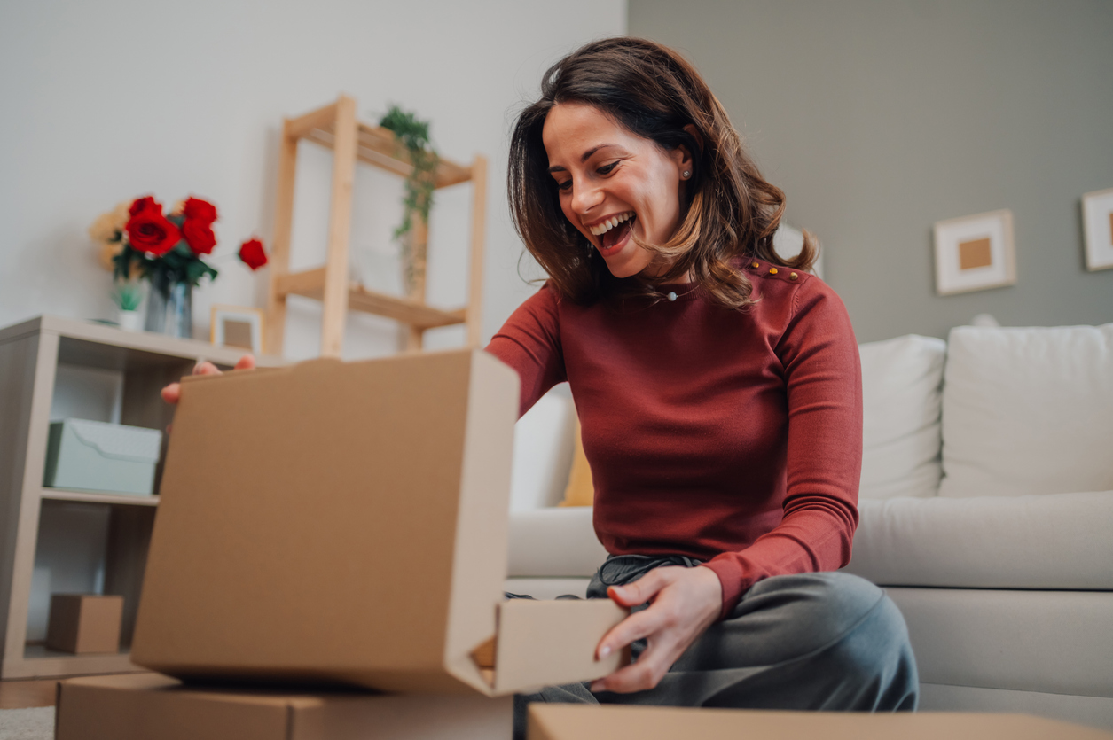 Mujer feliz abriendo un paquete en casa, descubriendo un regalo