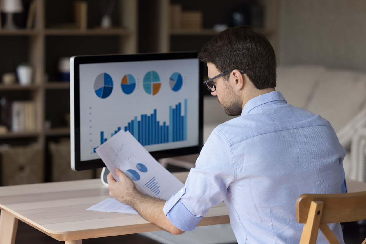 Hombre de negocios millennial enfocado que analiza informes de marketing en monitor de escritori
