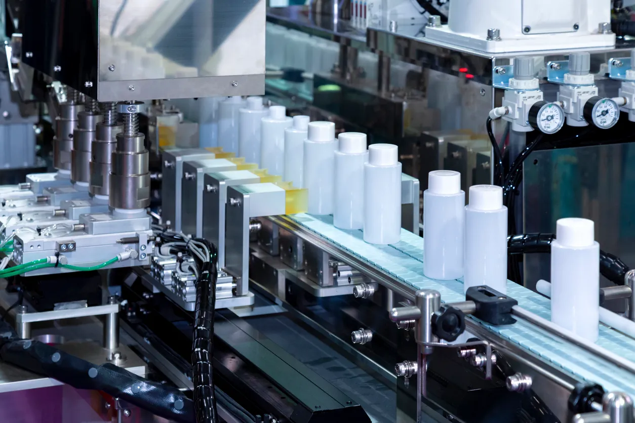 Botella de plástico blanca desplazándose sobre una cinta transportadora de una máquina automática de taponado y etiquetado