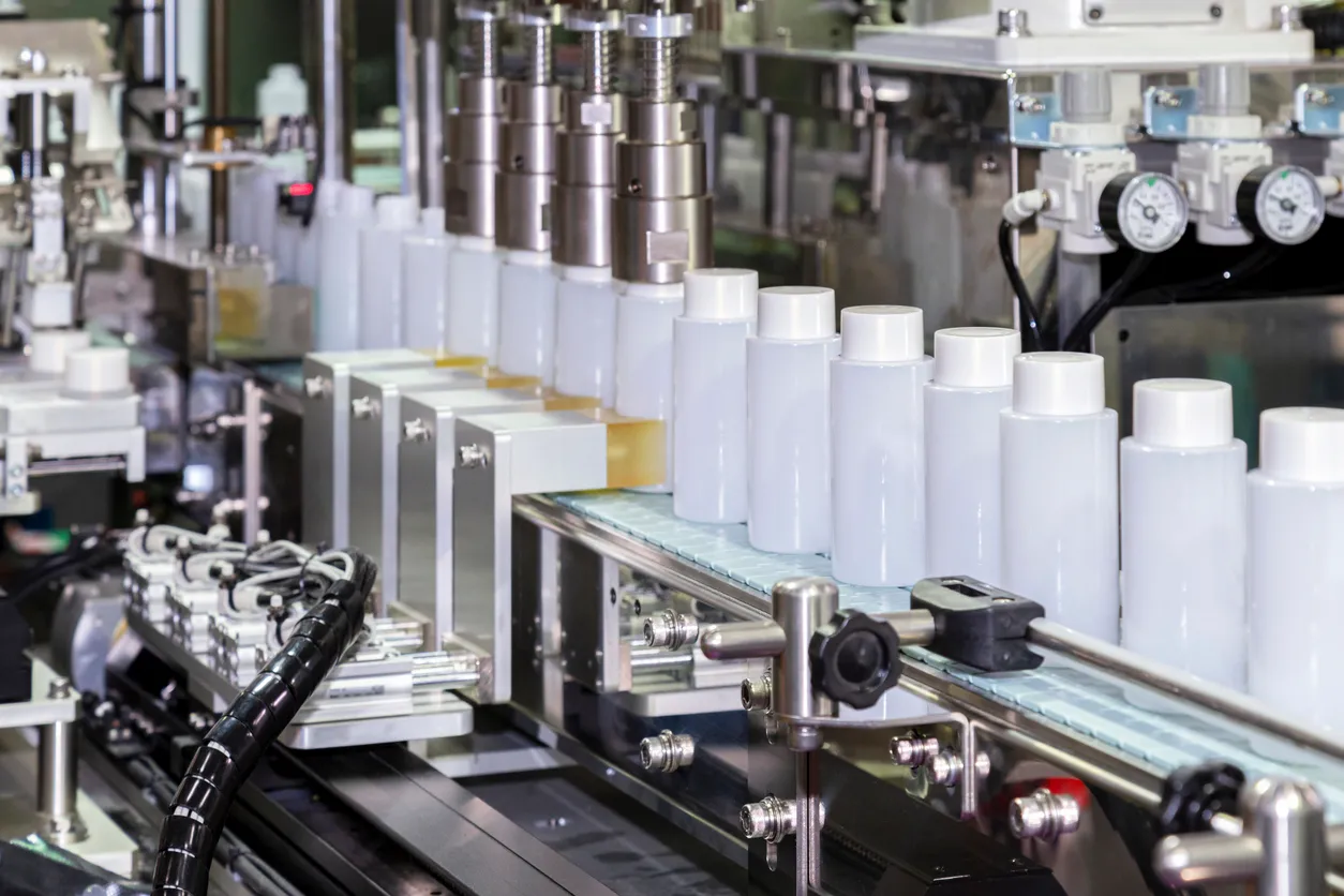 Botella de plástico blanco que se mueve en la cinta transportadora de la máquina de tapado automático en industria cósmetica 