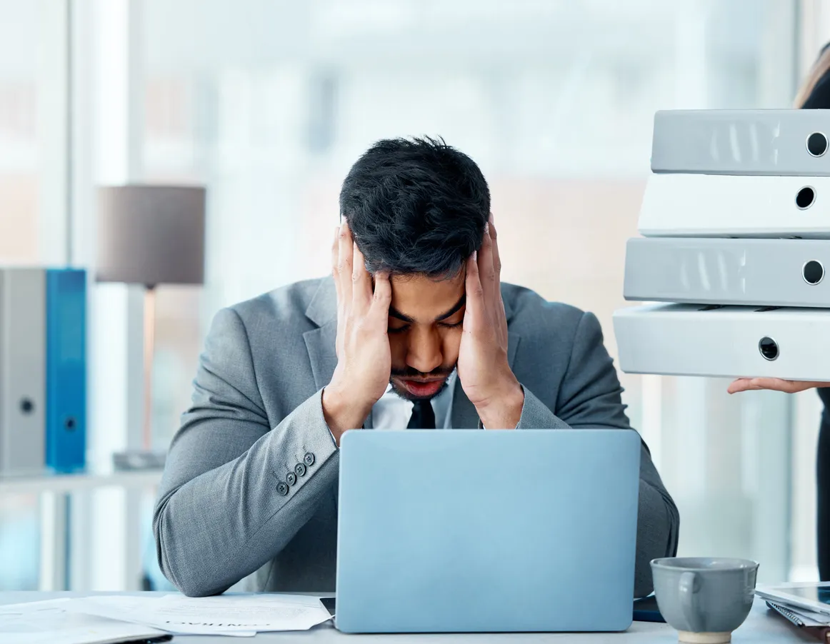 joven empleados en su ofician tomandose la cara con ambas manos, mostrando estres