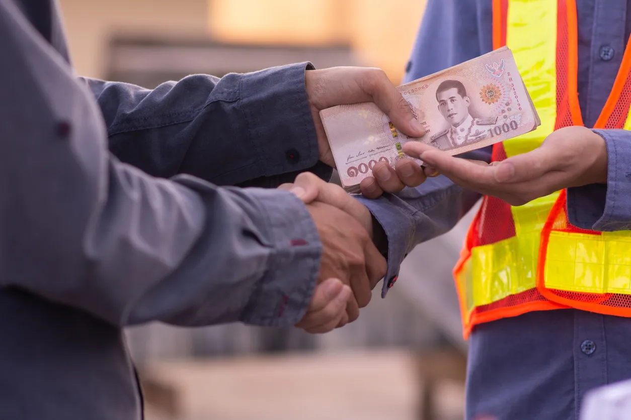 Empleado entregando su aguinaldo a trabajador con chaleco de seguridad