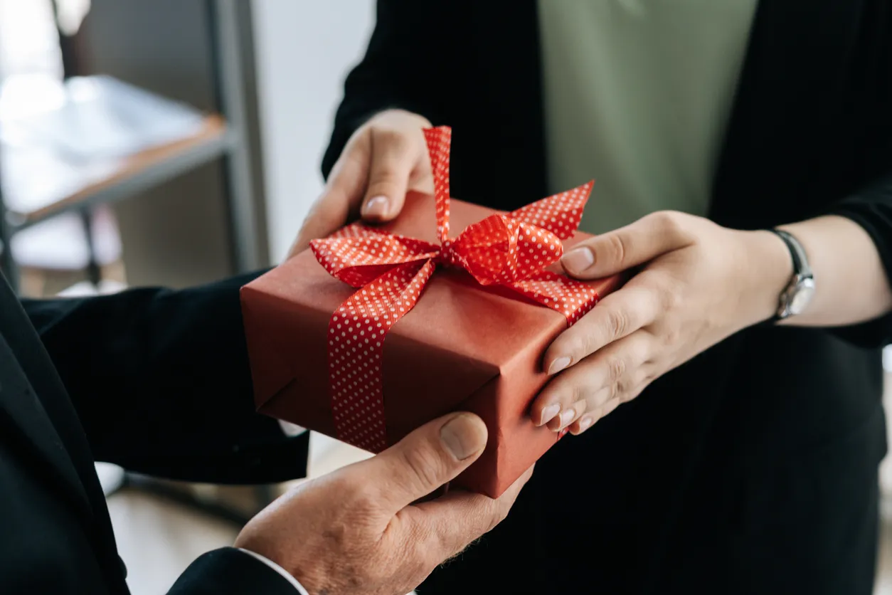 Vista de cerca de las manos de una mujer irreconocible dando caja de regalo roja atada a la proa entregado al hombre