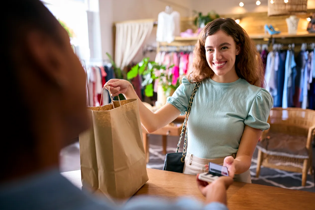 Cliente femenina en tienda de moda que paga por ropa con la aplicación de pago de teléfono móvil sin contacto
