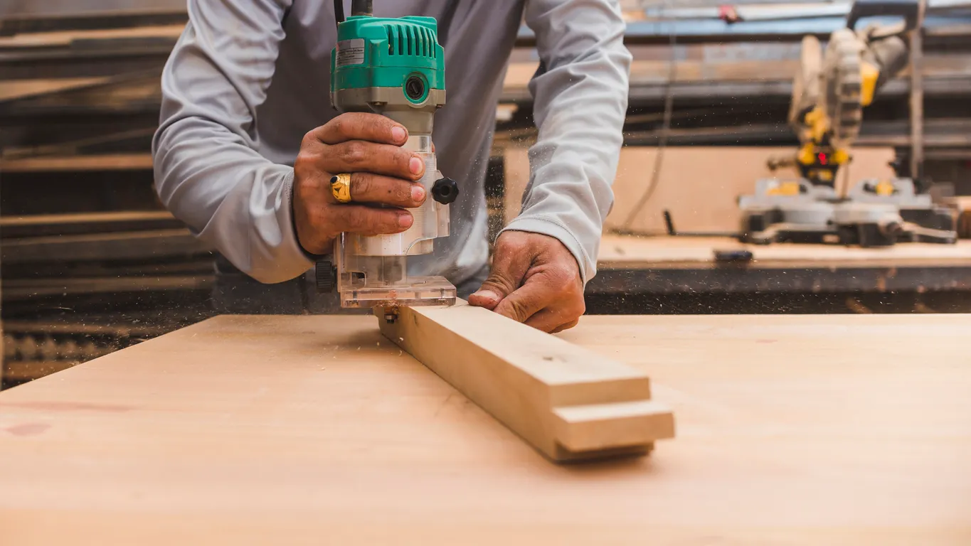 Un carpintero utiliza una recortadora de madera para chaflán en el borde de una pata de mesa
