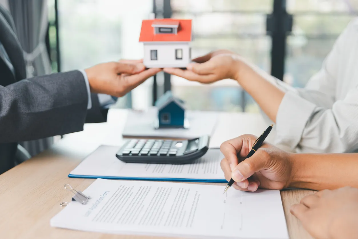 Dos personas tomando una pequeña casa con uno de sus manos, simulando la entrega de una casa. 
