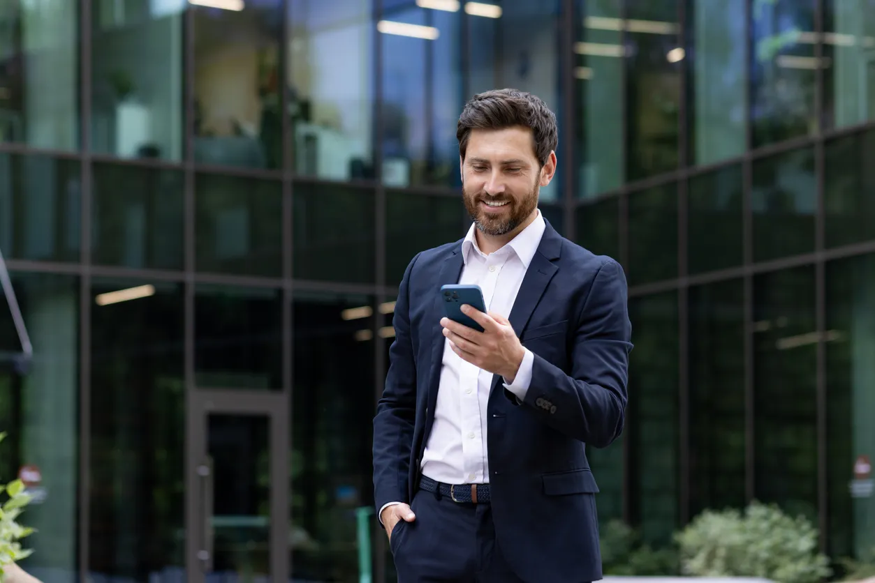 Hombre de negocios seguro que usa un teléfono inteligente en un entorno corporativo urbano.