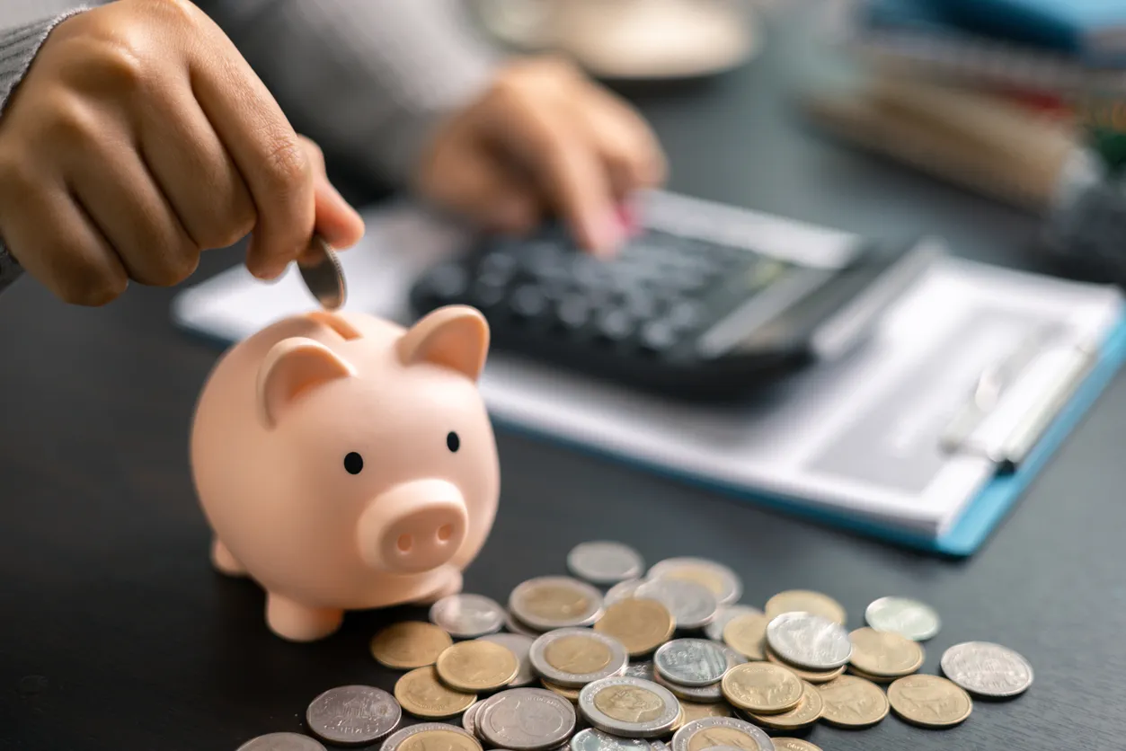 Financiero realizando calculos y con una alcancía y monedas a su alrrededor