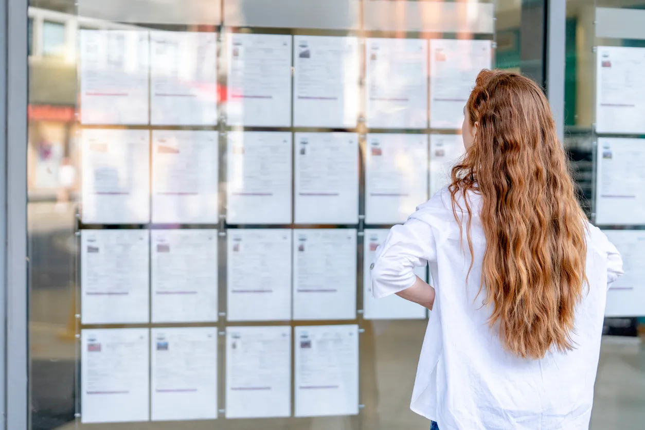 Mujer joven examina listados de trabajo publicados afuera de un edificio en un área urbana concurrida durante el día 