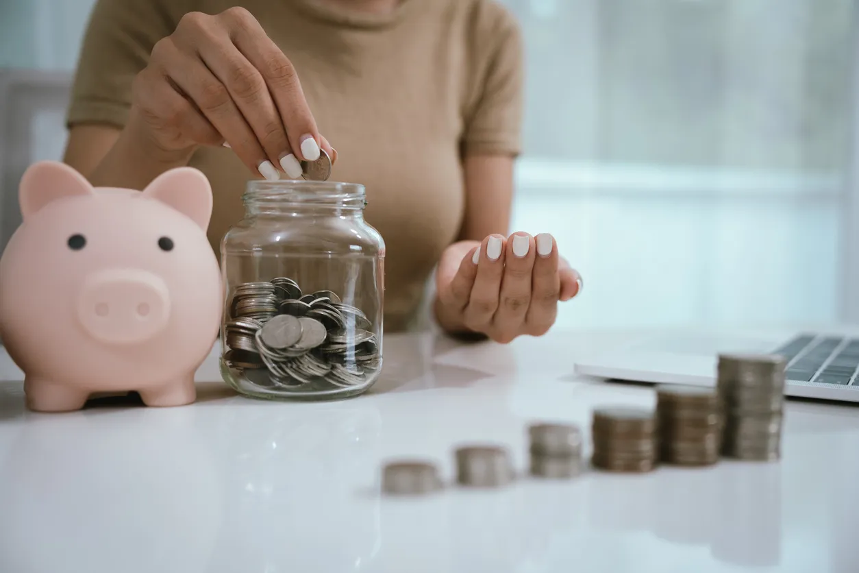 Una mujer asiática planea dividir su dinero en monedas y una alcancía, simbolizando la elaboración de presupuestos