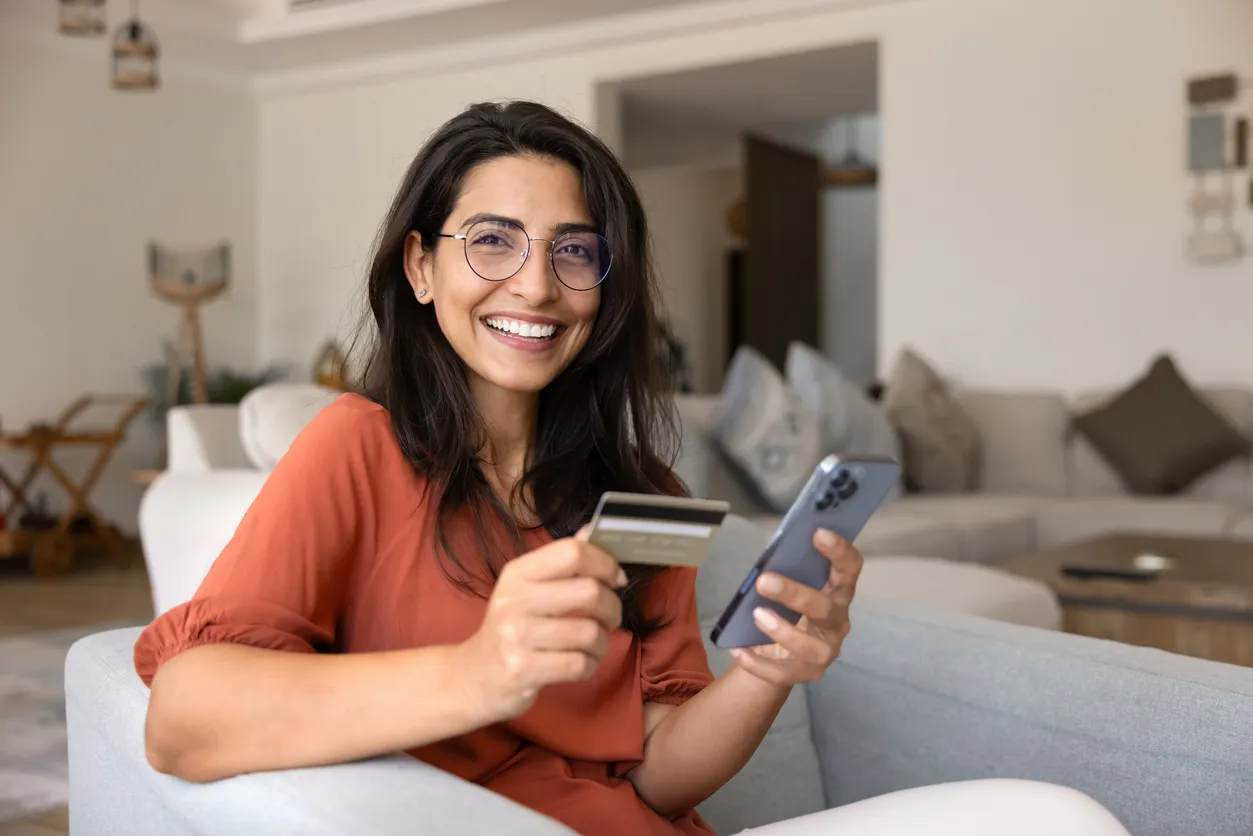 Mujer hispana joven feliz usando teléfono móvil y tarjeta de crédito