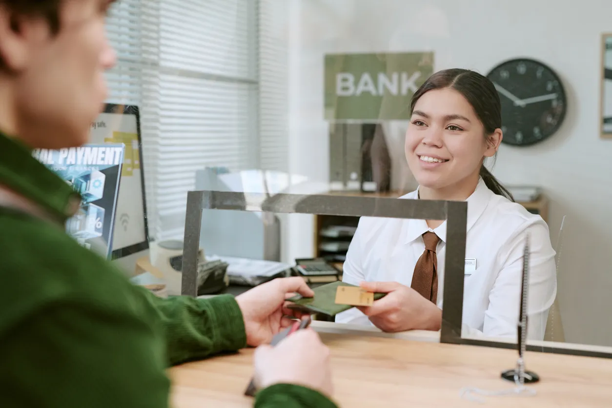 Persona en caja de un banco  siendo atendido por empleada alegre