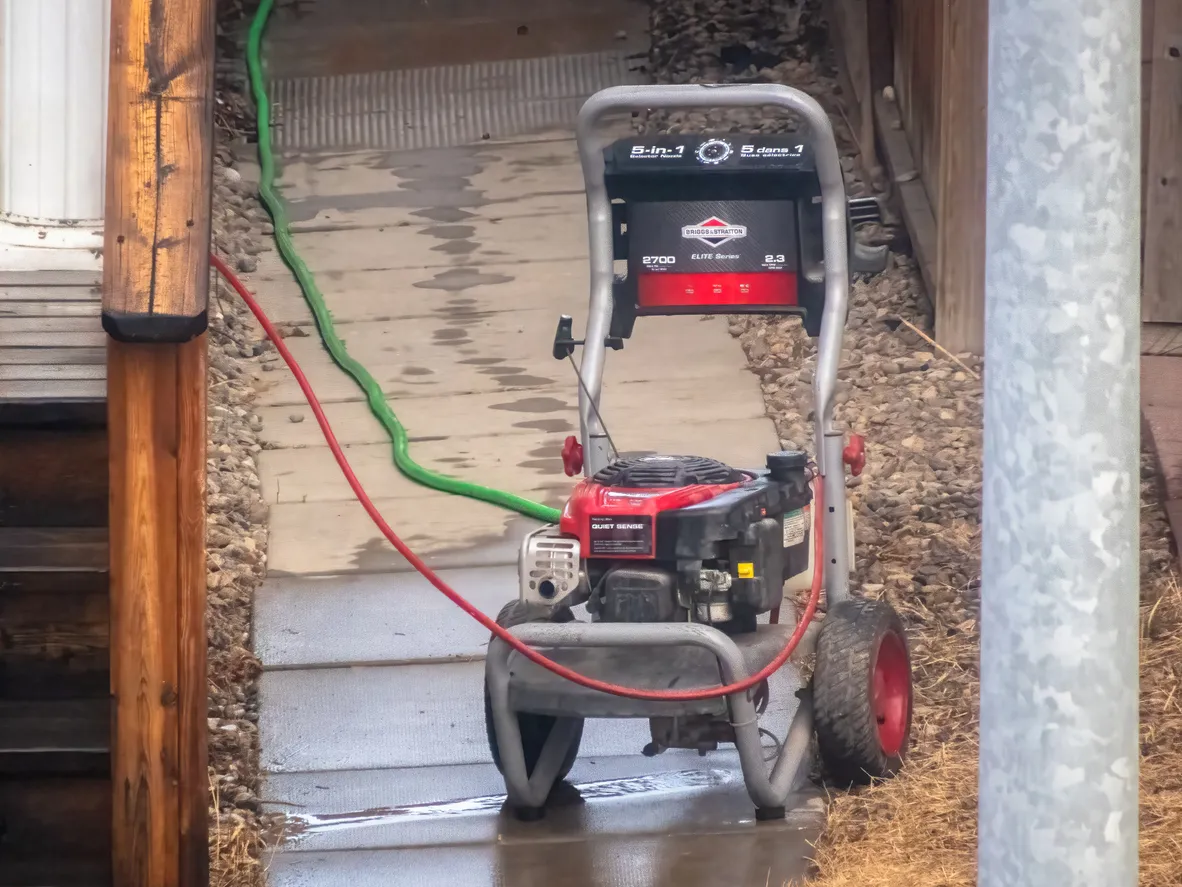 Una lavadora a presión de Briggs and Stratton se encuentra en un camino de concreto húmedo, con una manguera verde a su lado