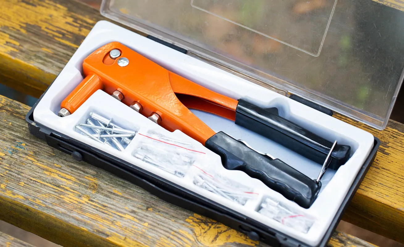 Kit de herramientas con remachadora manual naranja y sujetadores sobre una superficie de madera a la luz del día 