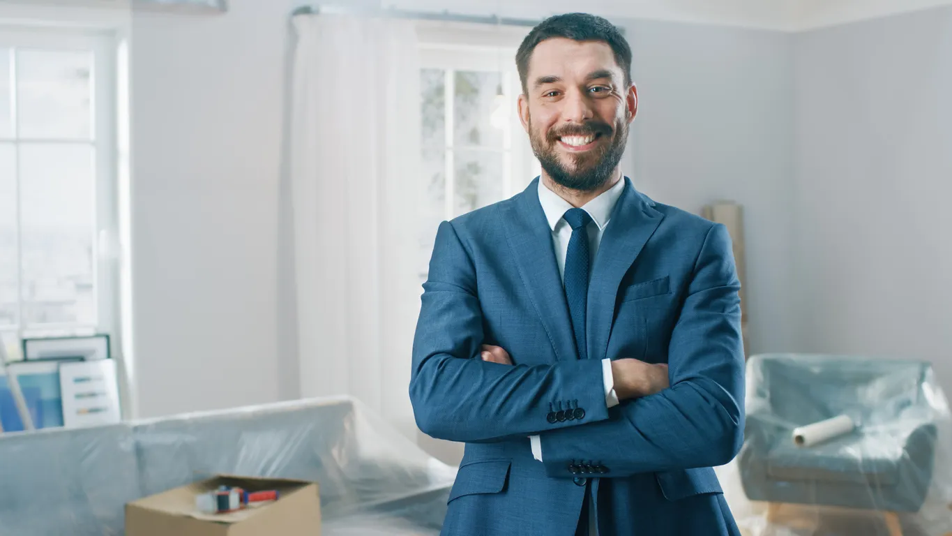 Agente inmobiliario exitoso en un traje sonrisas y ofrece las llaves de un nuevo apartamento. De pie en el medio de la habita