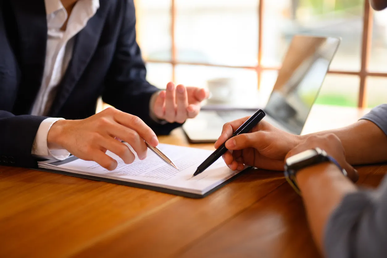 Primer plano abogado o agente de seguros señalando el contrato que muestra al cliente masculino dónde firmar