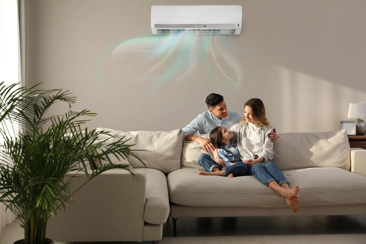 Familia feliz descansando bajo el aire acondicionado en una pared beige en casa