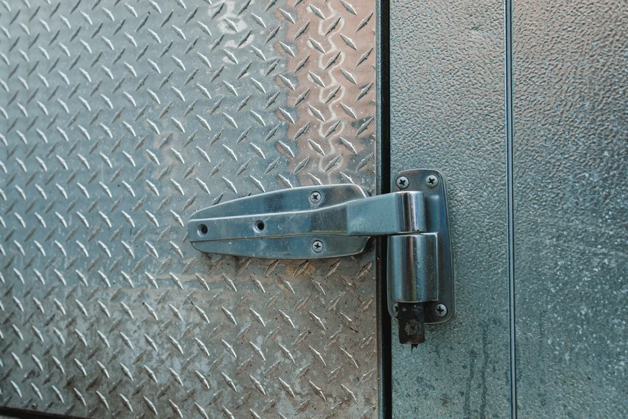 Bisagra metálica en una puerta de chapa diamantada en una obra durante el día en una zona urbana -