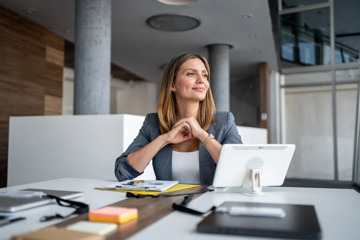 Mujer de negocios sonriendo y mirando hacia otro lado mientras está sentada en el escritorio