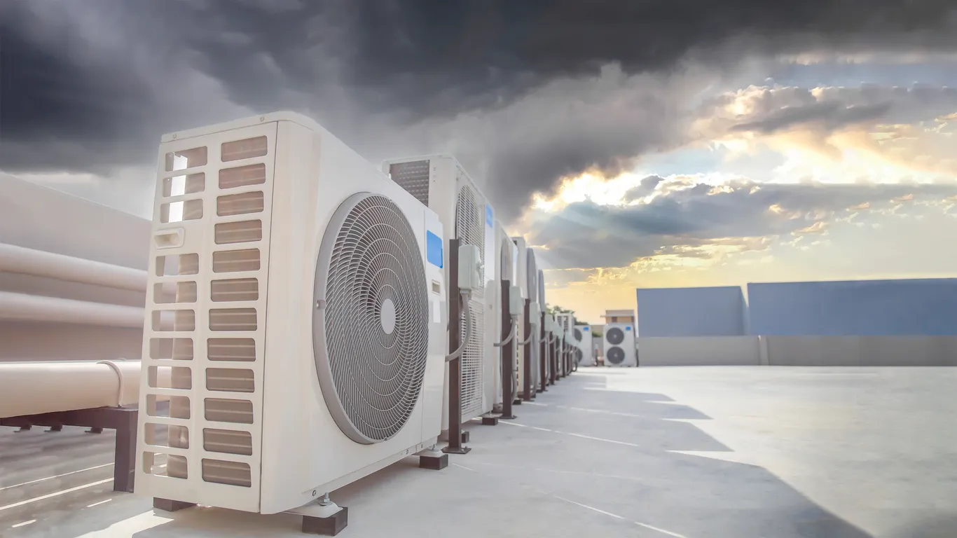 Aire acondicionado (HVAC) en el tejado de un edificio industrial con cielo azul y nubes.