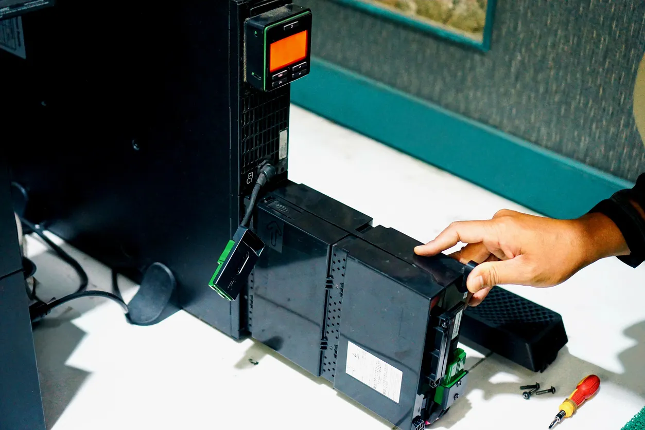 Un hombre instalando un paquete de baterías de repuesto para una fuente de alimentación ininterrumpida, o UPS. 