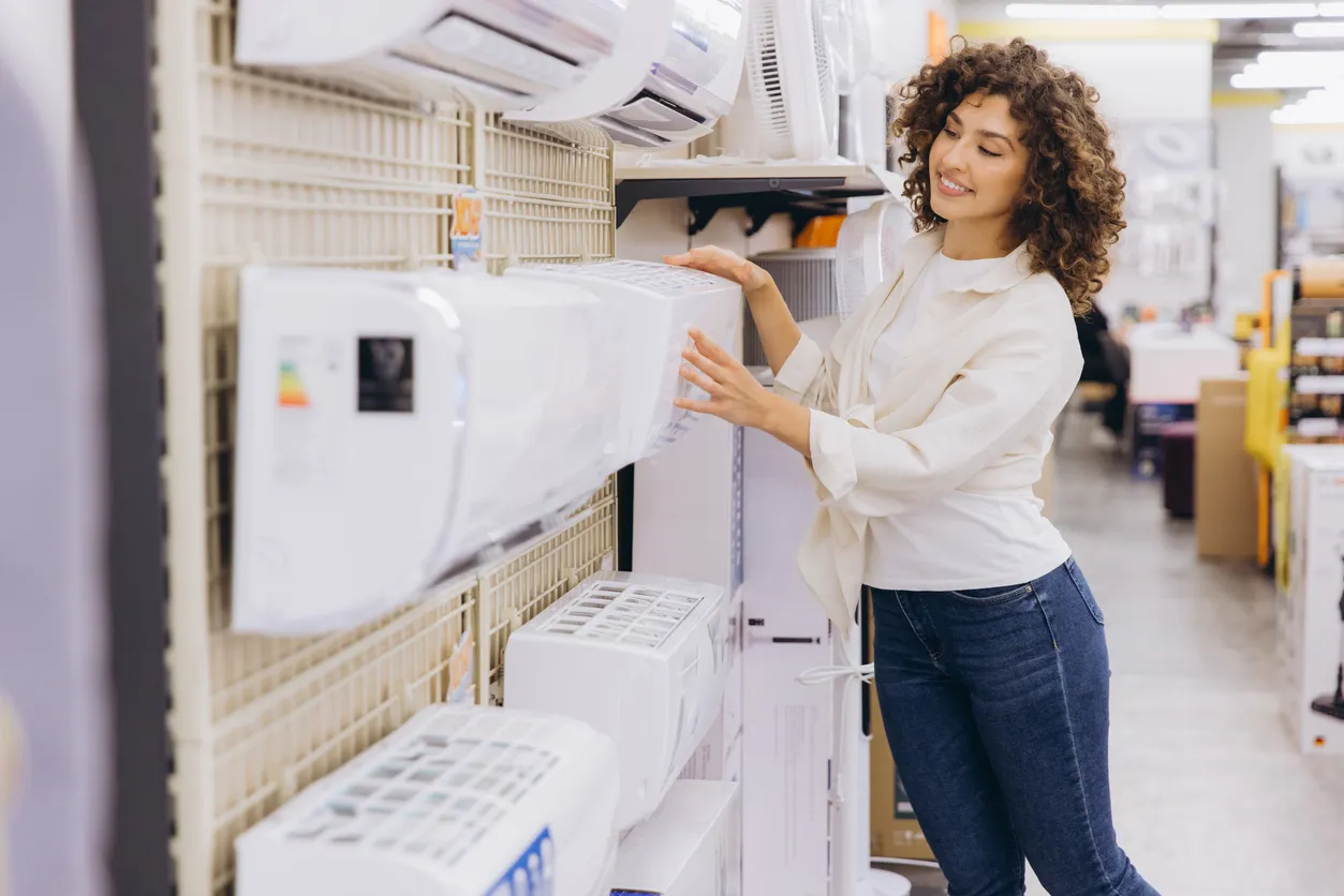 Cliente seleccionando un aire acondicionado en una tienda de electrodomésticos, examinando diferentes modelos en exhibición