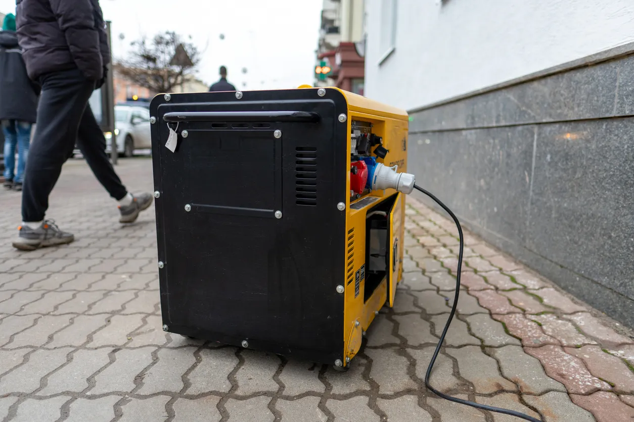 Generador colocado en la acera cerca de personas, mostrando su cable de alimentación conectado