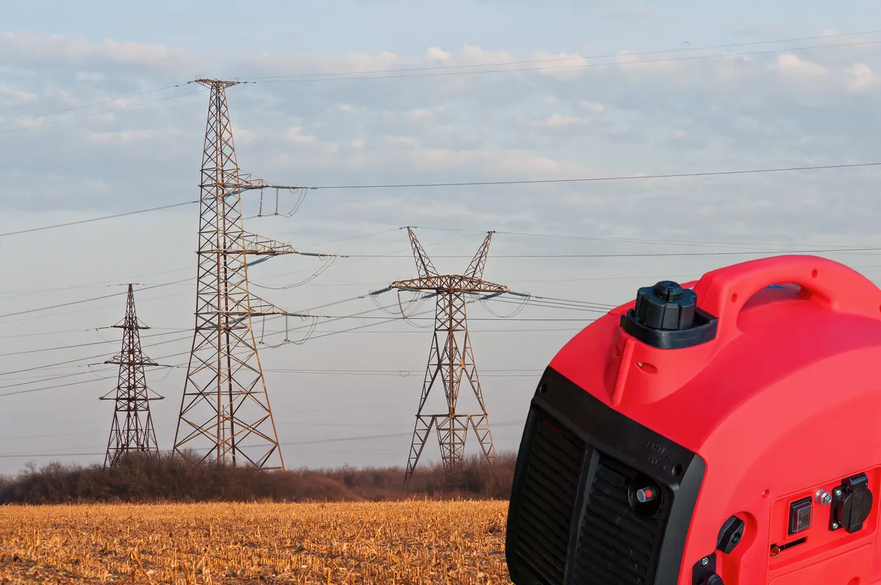 Generador portátil rojo en un campo con líneas eléctricas de alta tensión al fondo