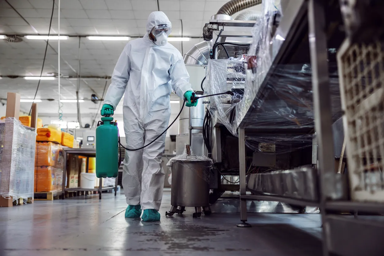 Hombre con traje de protección y mascarilla desinfectando un almacén lleno de productos alimenticios