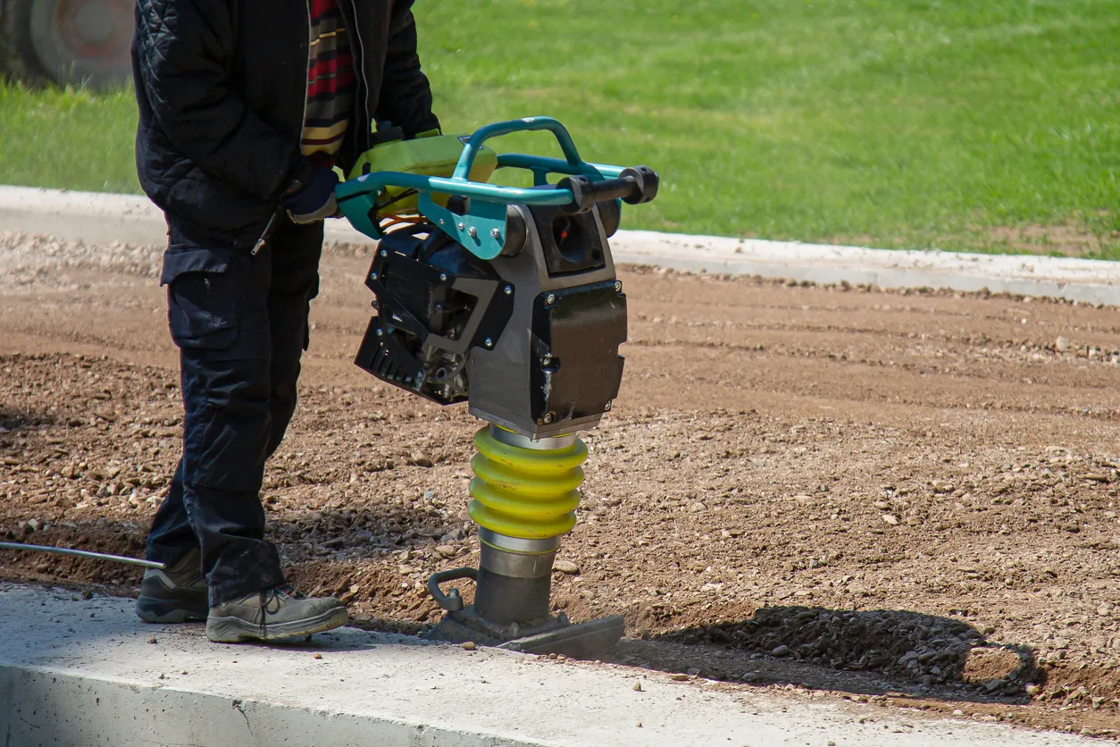 Un trabajador de la construcción endurece un terreno arenoso con un apisonador vibratorio.