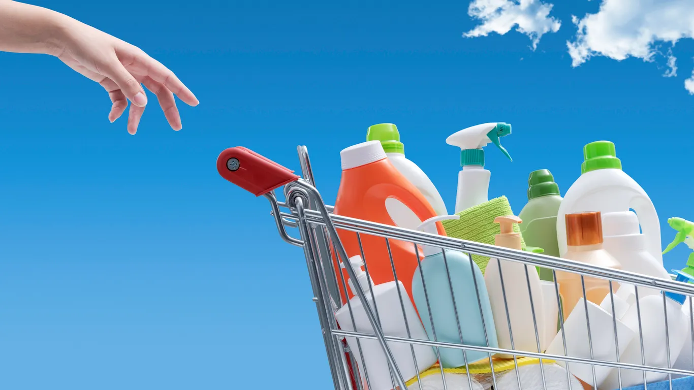 Mujer comprando detergentes: carrito de compras lleno de botellas de detergente y cielo azul al fondo