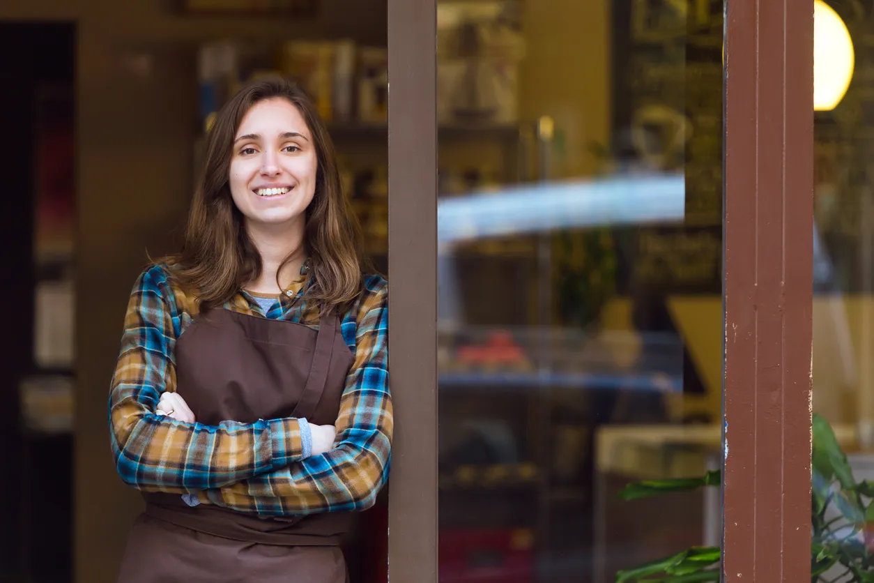 Hermosa vendedora joven mirando a cámara y apoyado contra el marco de la puerta de una tienda de orgánico