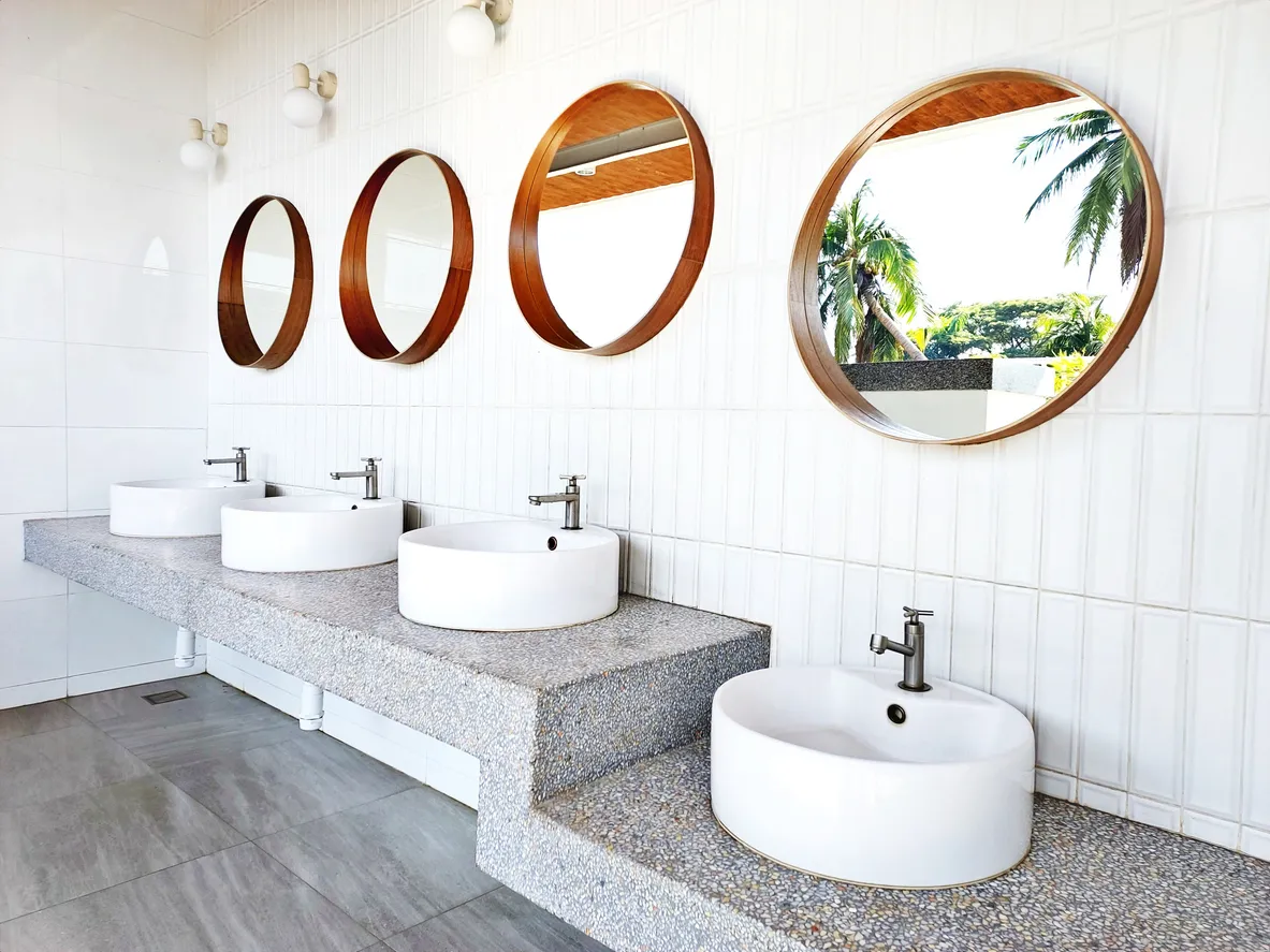  85 / 5.000 Espejo redondo de diseño para baño al aire libre sobre pared de cerámica, lavabo blanco sobre estante de granito.