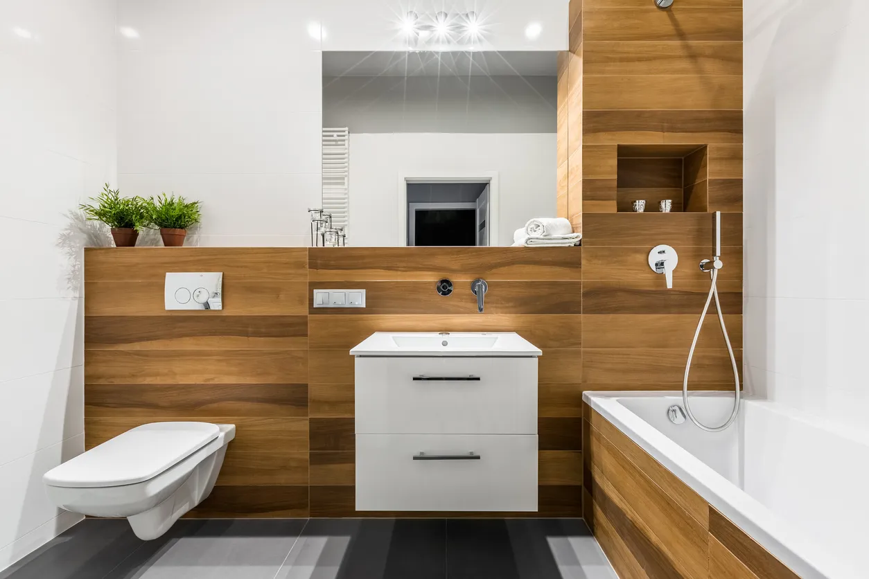 Baño moderno de madera con bañera, espejo, inodoro, mueble y lavabo.