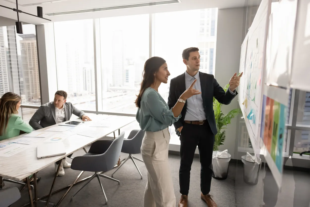 Colegas de negocios enfocados hablando en el tablero Kanban con notas adhesivas 
