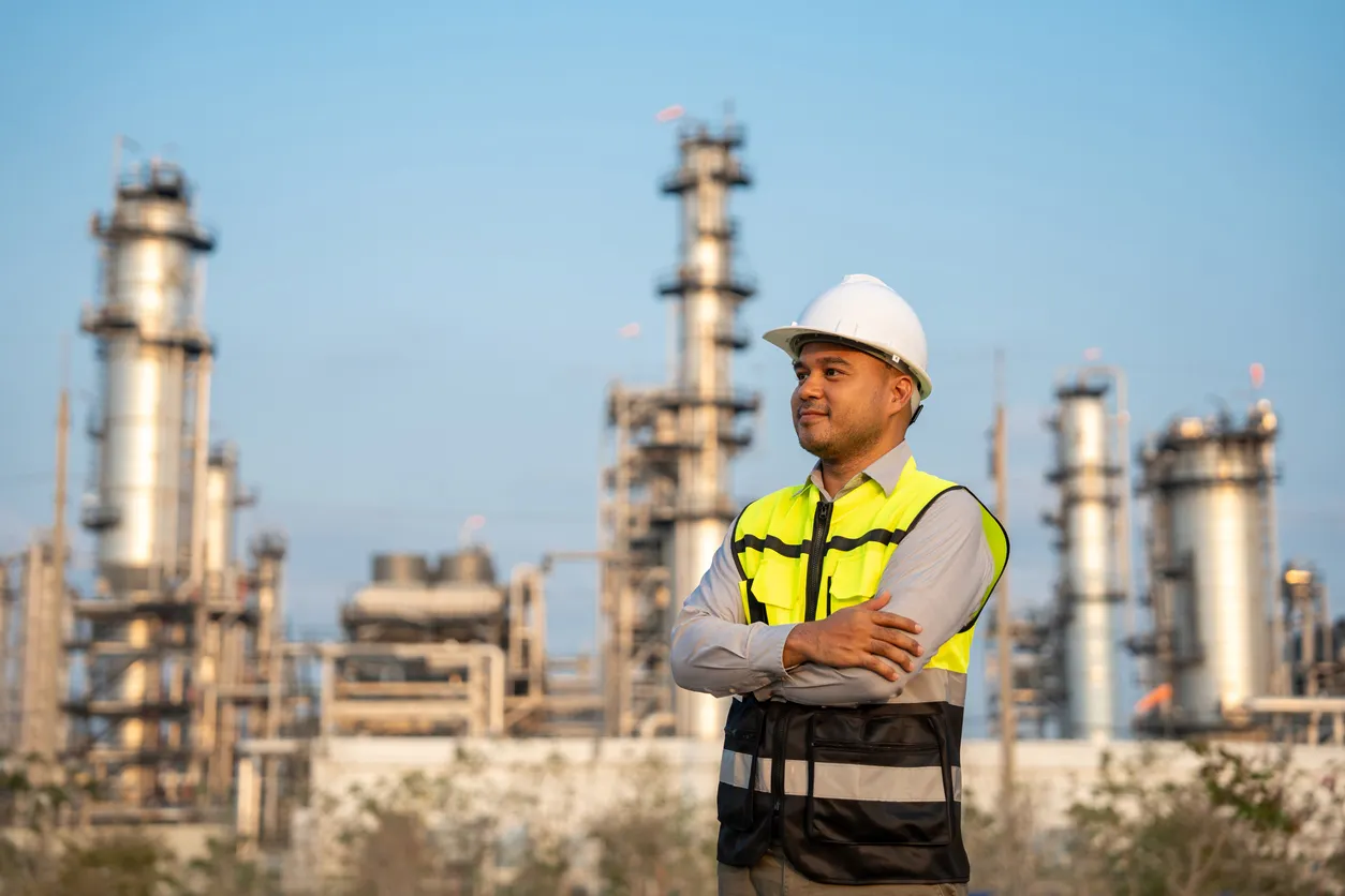 Ingeniero asiático con casco de seguridad de pie frente a la refinería de petróleo. Zona industrial gas petroquímica