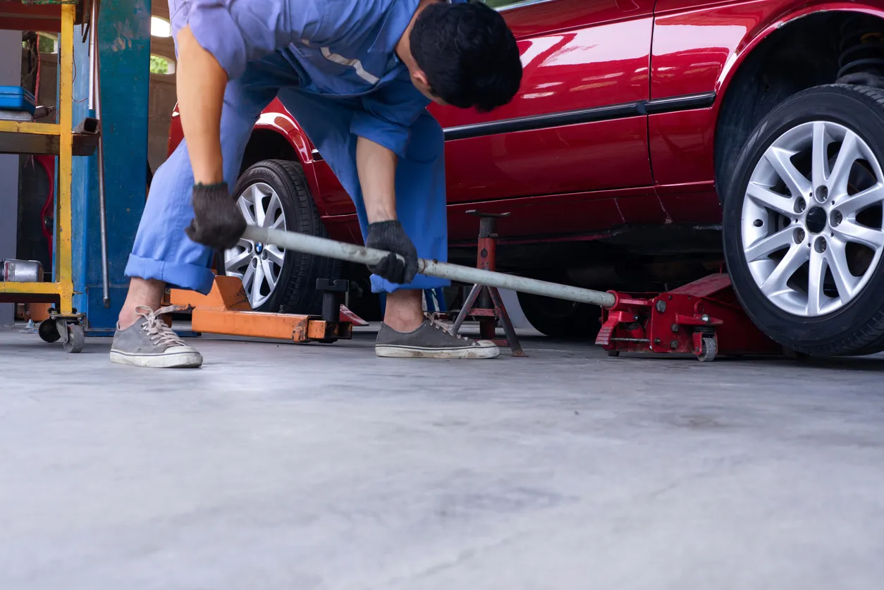 Un técnico asiático usa un gato para levantar el coche del suelo