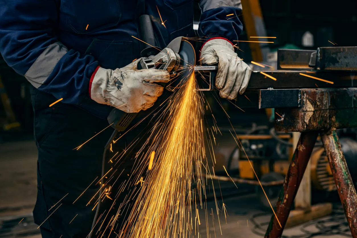 Primer plano de un trabajador de la metalurgia moliendo piezas metálicas en una fábrica de la industria pesada. 