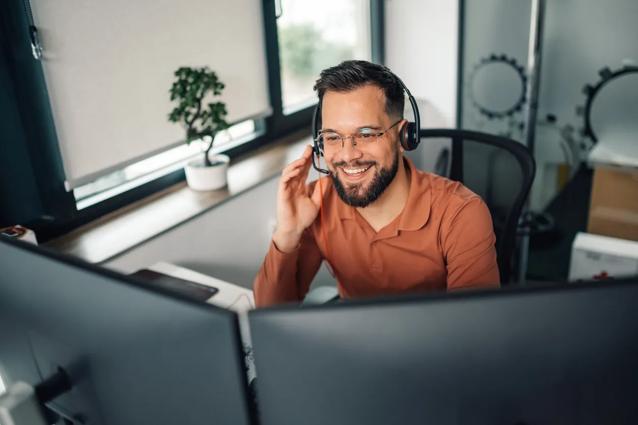 Representante de servicio al cliente sonriente que trabaja desde la oficina en casa usando auriculares y monitores duales