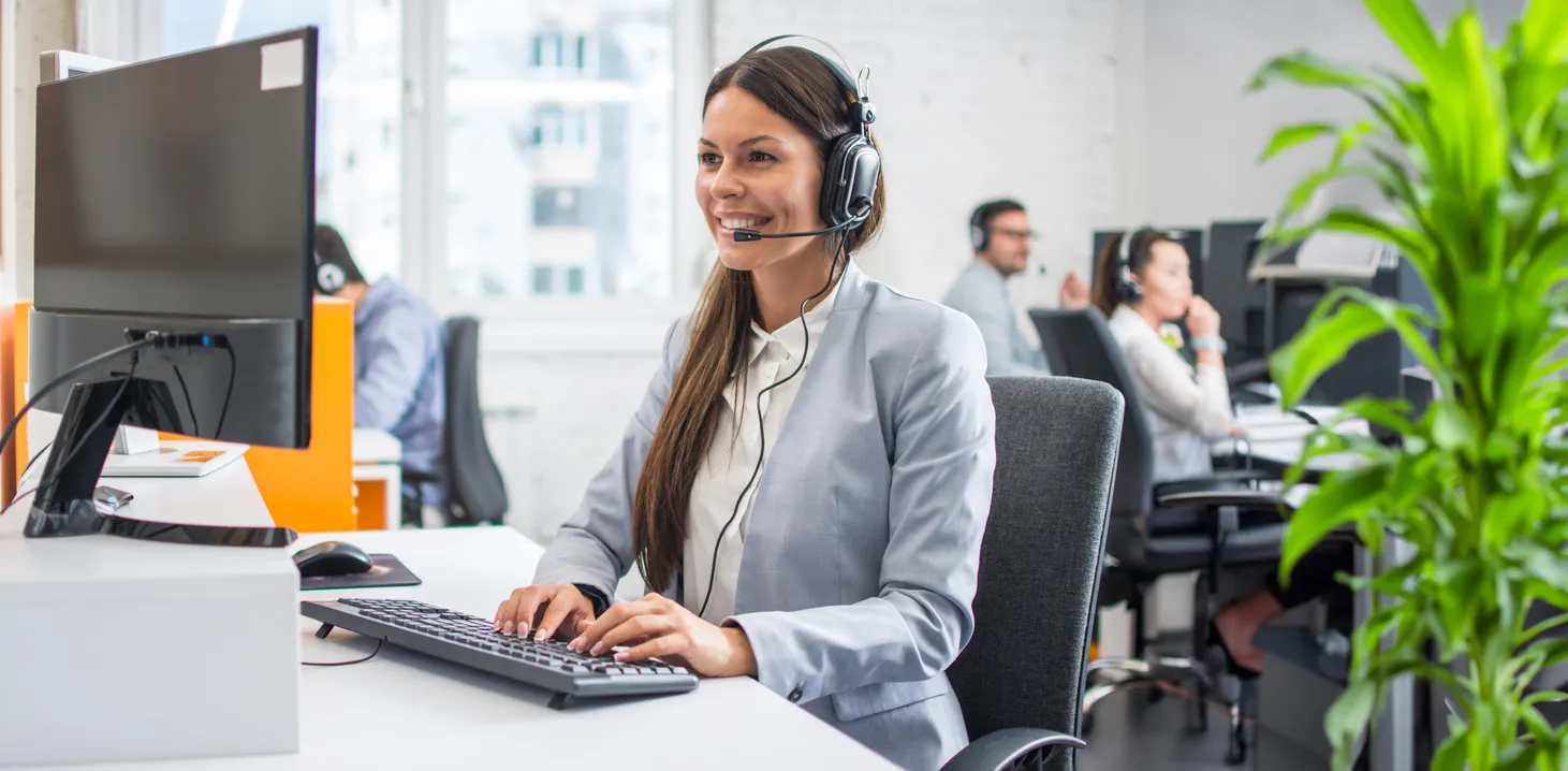 Hermosa joven representante de servicio al cliente que usa auriculares que trabajan en la computadora en la oficina del centr