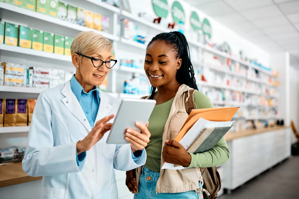 Farmacéutica mayor y joven mujer negra usando touchpad en una farmacia