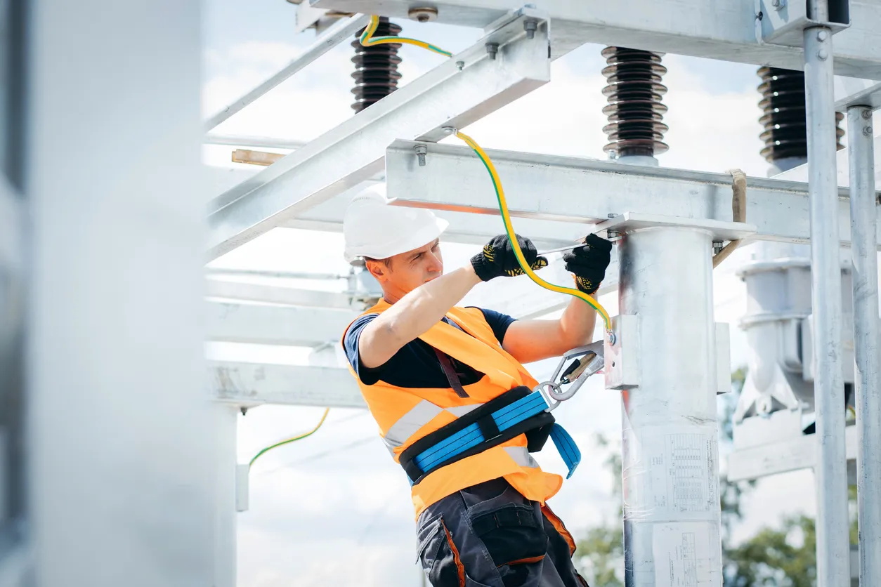 Electricista con casco protector trabajando en líneas eléctricas de alta tensión.