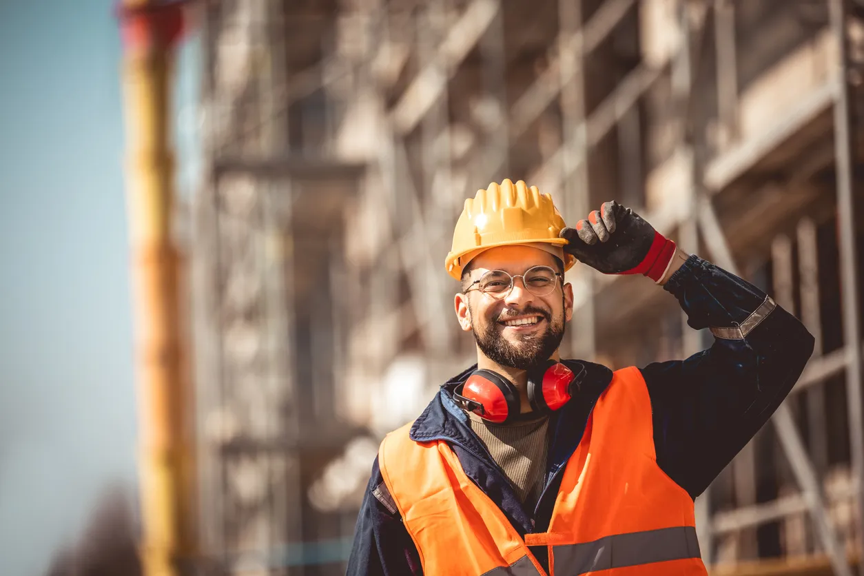 Gerente de obra de construcción de pie con chaleco de seguridad y casco, pensando en la obra.