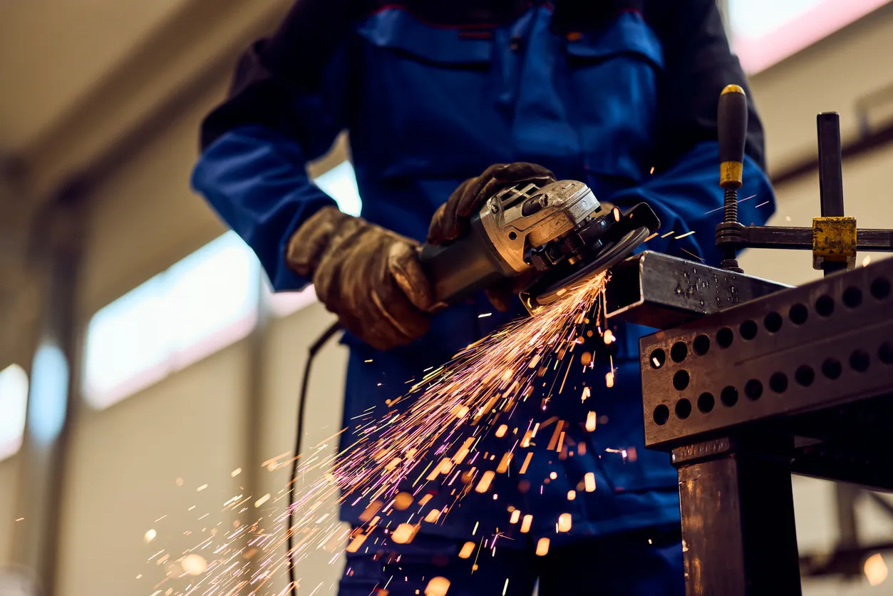 Trabajador cortando metal con amoladora angular que produce chispas brillantes en el taller 