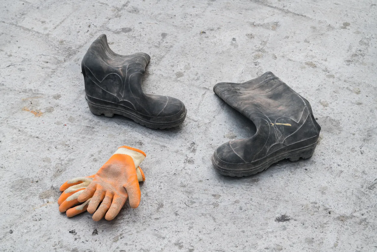 Botas de goma sucias y guantes de trabajo sobre suelo de hormigón