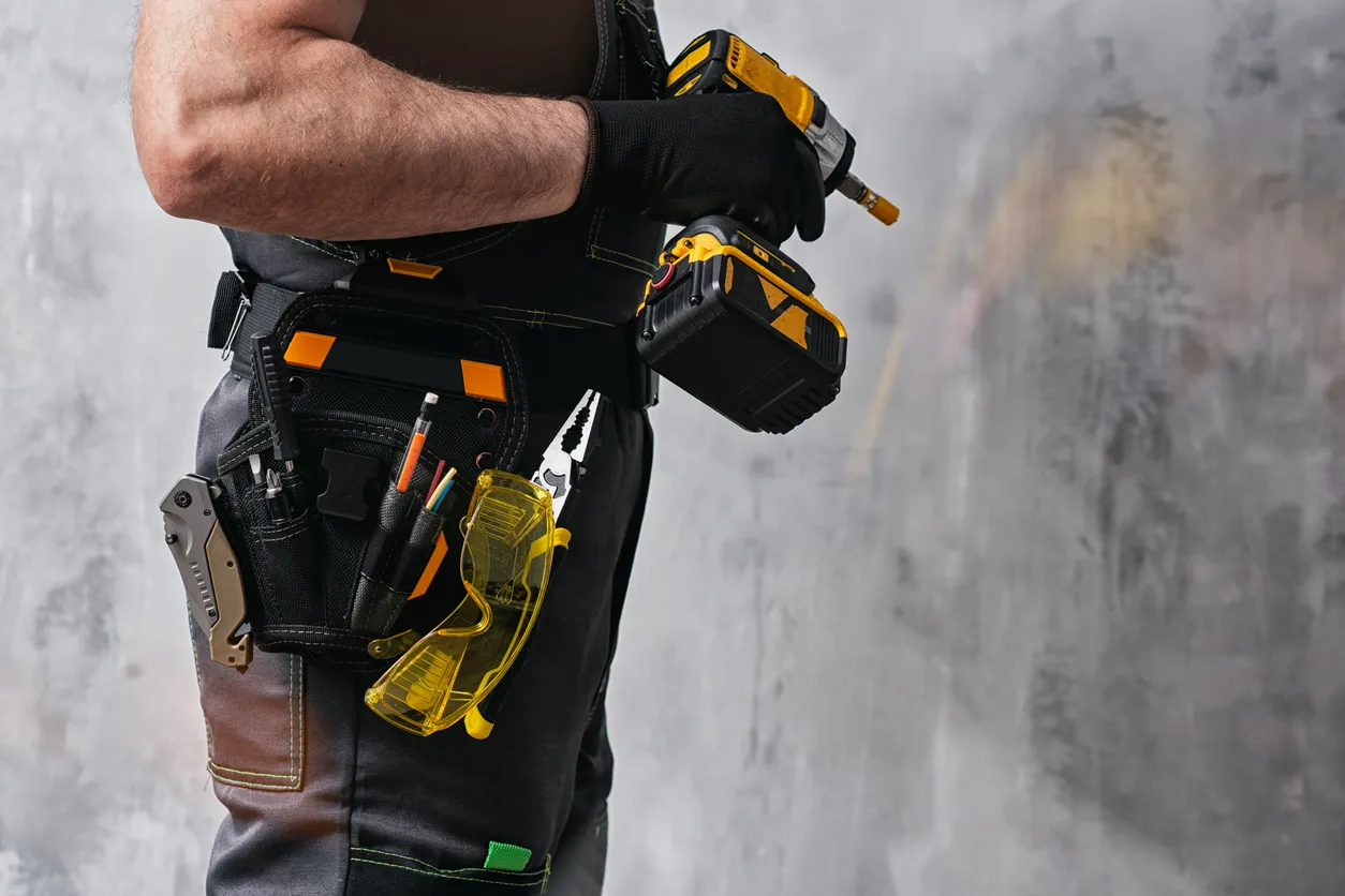 Trabajador de la construcción uniformado sosteniendo un destornillador inalámbrico de color amarillo