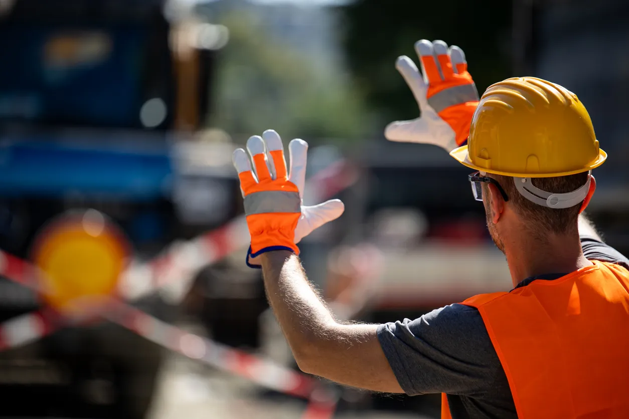 Trabajador de la construcción dirigiendo el tráfico en un sitio concurrido por la tarde bajo un cielo despejado durante el tr
