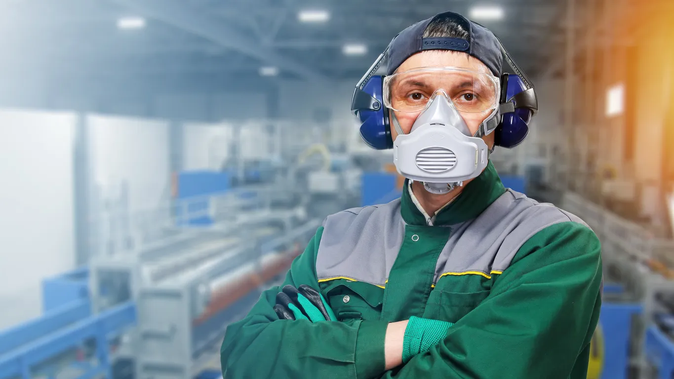 Trabajador con ropa protectora, auriculares y respirador se encuentra en el contexto de la fábrica industrial 