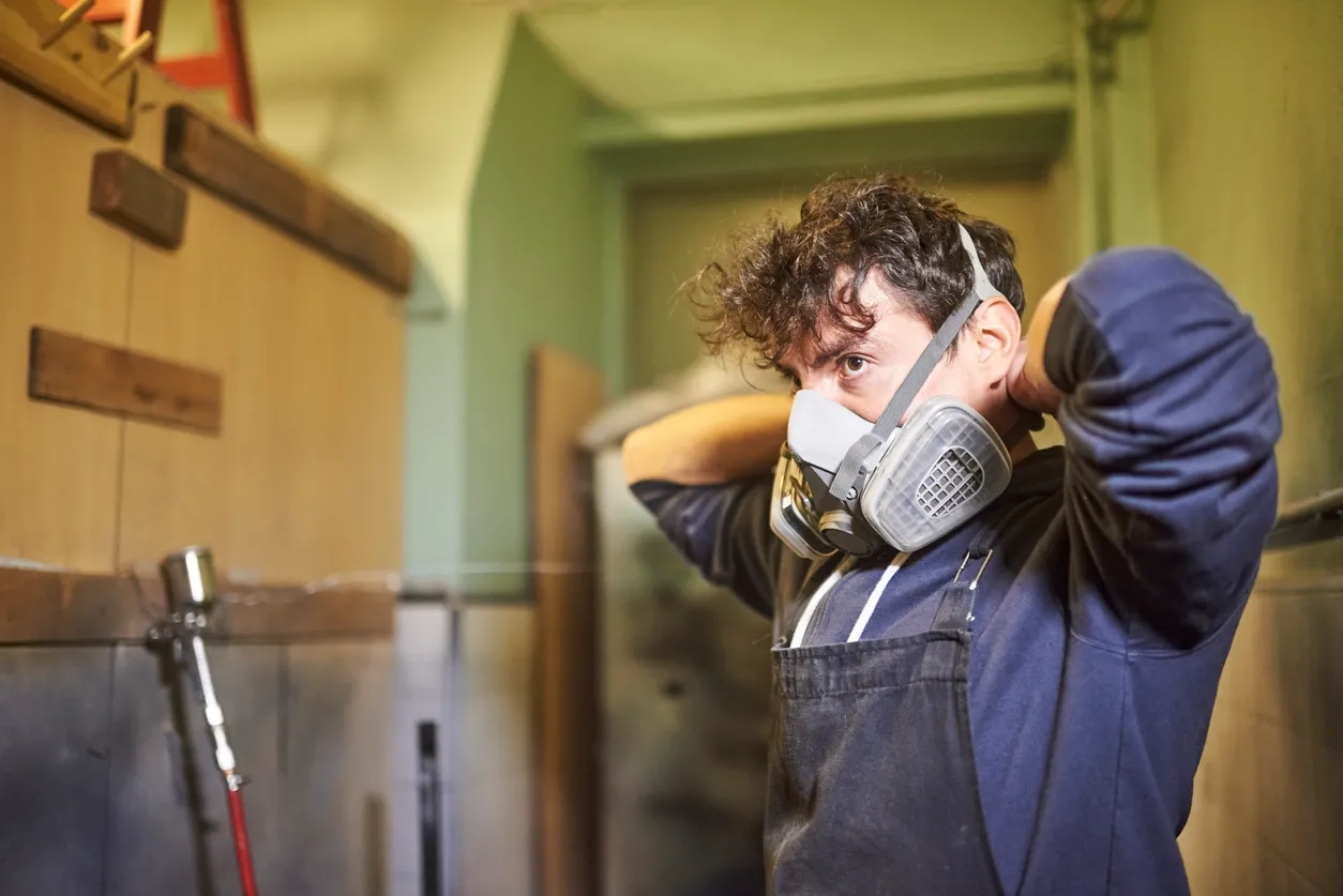 Un hombre se quita una máscara protectora de respiración mientras termina su trabajo de pintura con aerosol -